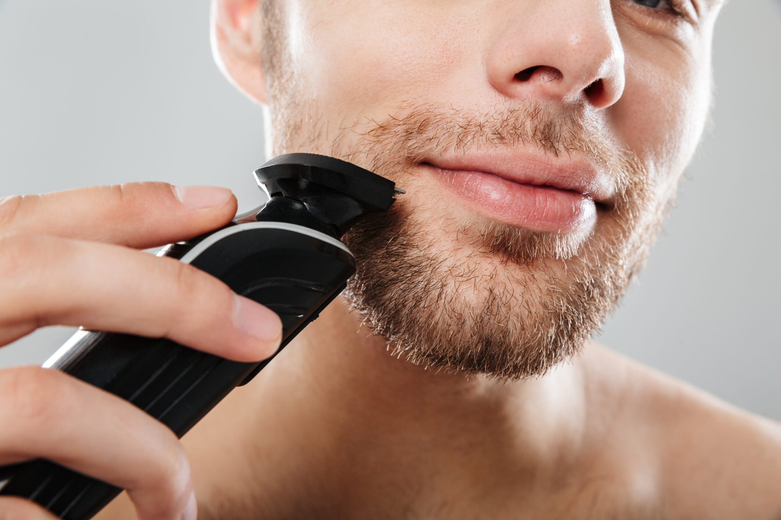 Close up shot of handsome man smiling while shaving his face wit close-up-shot-handsome-man-smiling-while-shaving-his-face-with-electric-shaver-making-morning-procedure-bathroom